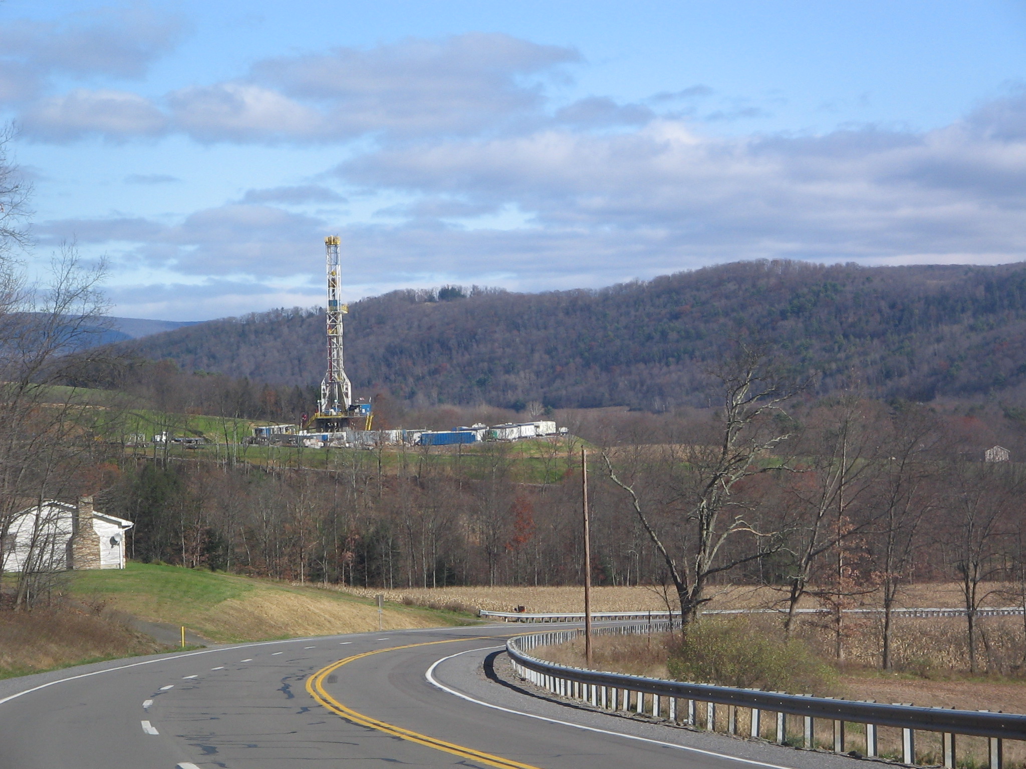 Marcellus shale gas drilling tower in Lycoming County, Pennsylvania, photographed in 2009. A tall steel rig with red and white stripes stands in a clearing surrounded by forest.